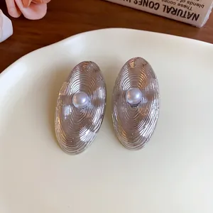 Primo piano di orecchini ovali color argento con superficie testurizzata e perla centrale