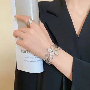 Close-up of textured metal flower bracelet and ring worn on hand with black blazer