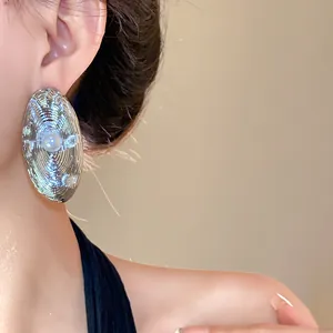 Orecchini ovali geometrici in argento con trama a onde e perla centrale su modella