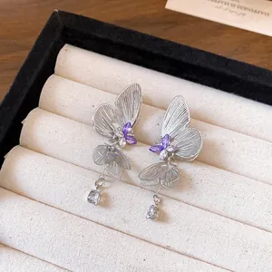 Detail of silver hollow butterfly earrings with purple crystals and teardrop tassel.