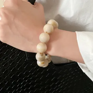Close-up of marbled cream beaded bracelet worn on wrist with black woven bag.