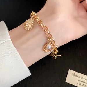 Vue détaillée d'un élégant bracelet en or avec des breloques coquillage et perle au poignet