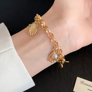 Vue détaillée d'un bracelet doré avec des breloques coquillage et perle sur un poignet