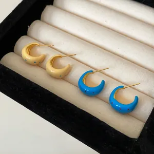 Detailed view of C-shaped enamel hoop earrings with polka dot patterns in a jewelry box.