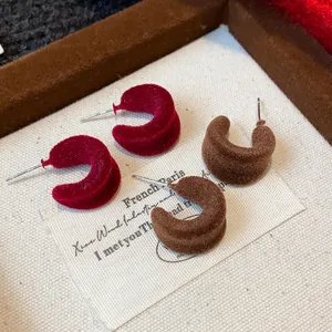 Primo piano di eleganti orecchini floccati a forma di C nei colori rosso vino e marrone