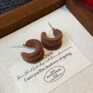 Dettaglio macro di orecchini a bottone a C floccati marroni con texture vellutata