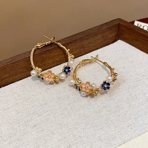 Close-up view of elegant gold hoop earrings featuring enamel flowers and white pearls