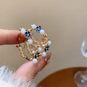 Detail view of elegant gold floral hoop earrings with pearls and blue enamel petals