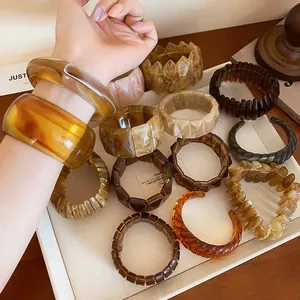 Close-up of assorted amber and marbled resin bangles displayed on a minimalist tray