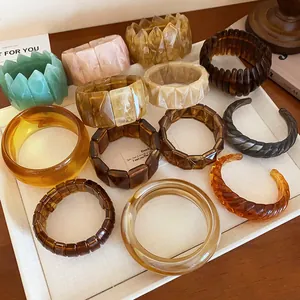 Various marbled and geometric resin bracelets displayed on a textured white board