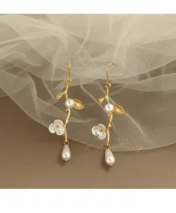 Dettaglio di eleganti orecchini a ramo dorato decorati con fiori bianchi e perle