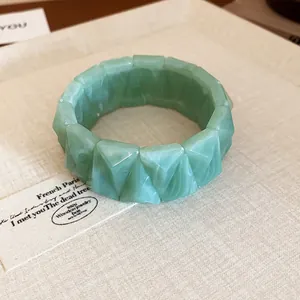 Detail view of the faceted green marbled resin bracelet displayed on a textured surface