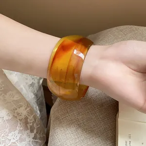 Detailed view of a chunky amber marbled resin open bangle worn on a female wrist