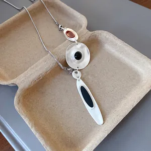 Detail showing irregular silver pendants with black drip oil on a minimalist snake chain