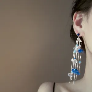 Close-up of blue acrylic flower tassel earrings worn on ear with silver chains.