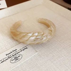 Detail of a beige marbled twisted resin cuff bracelet on a textured background.