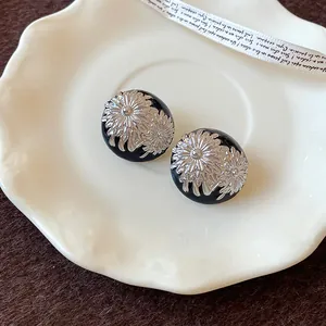 Detalle de cerca de pendientes vintage de esmalte negro con patrones florales plateados.