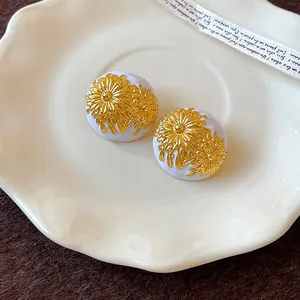 Primer plano de aretes vintage de esmalte blanco con motivos de margaritas doradas grabados