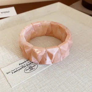 Close-up of pink marbled resin geometric faceted bangle bracelet on textured background