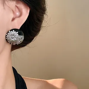 Primer plano de pendientes vintage de esmalte negro con diseño floral plateado