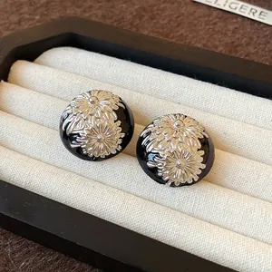 Primer plano de pendientes vintage de esmalte negro con relieve floral de margaritas
