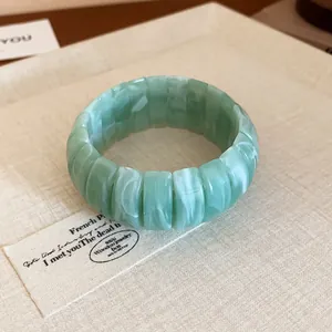 Green marbled resin block bangle shown in a detailed close-up with vintage prop background