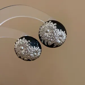 Primer plano de pendientes vintage de esmalte negro con diseño floral plateado.