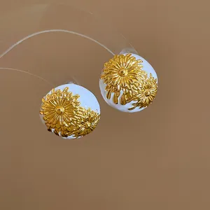 Detalle de los pendientes redondos blancos de estilo vintage con diseño floral dorado.