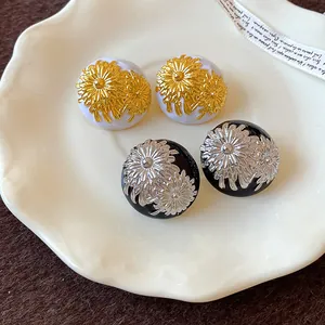 Primer plano de pendientes de esmalte vintage con flores, acabados blanco-oro y negro-plata.