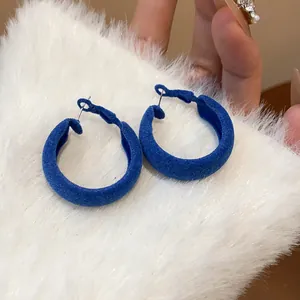 Macro view of blue flocked hoop earrings resting on soft white faux fur background