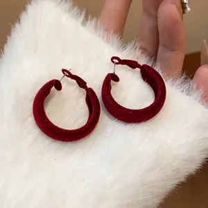 Close-up of red velvet flocked hoop earrings with elegant texture on white fur background.