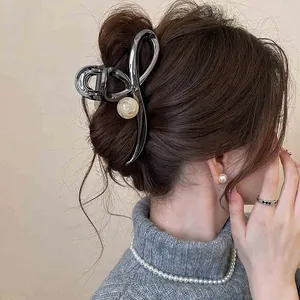 Elegant minimalist metallic hair claw clip with pearl accent worn on a classic bun hairstyle