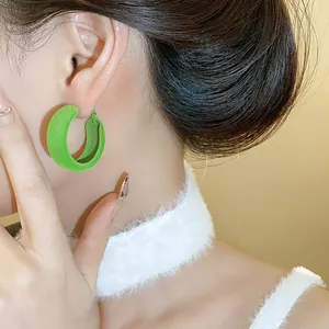 Detailed view of green flocked C-shaped hoop earrings worn with winter accessories.