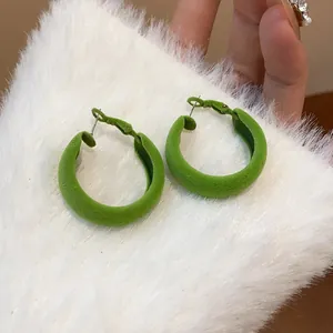 Macro detail of vibrant green flocked hoop earrings on white faux fur background