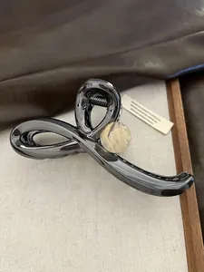 Detail showing a metallic crossover hair claw clip with a beige marble-patterned bead.