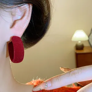 Close-up of red flocked round hoop earring on ear with warm indoor background