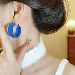 Close-up of blue flocked texture hoop earring on ear with warm indoor lighting background