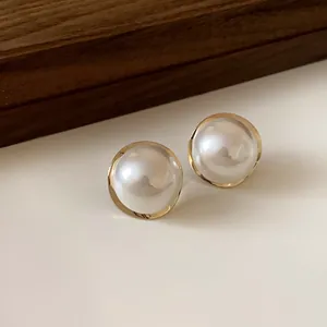 Elegant round pearl stud earrings with a gold-tone metallic frame on wooden background.