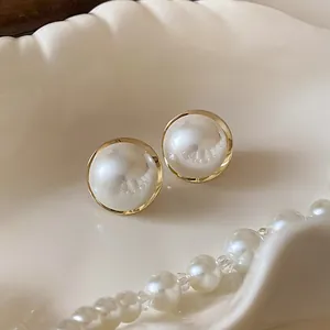 Elegant pearl stud earrings with a gold-tone rim displayed on a white shell dish