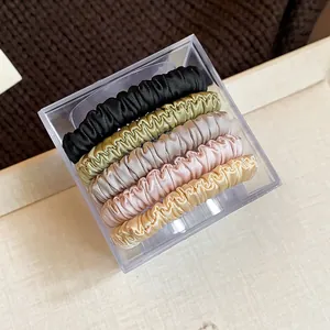 Detail of five satin fabric scrunchies in a clear box, featuring elegant earth tones.
