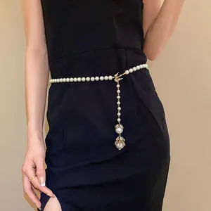 Detailed view of an elegant pearl waist chain with a gold bird pendant on a black dress