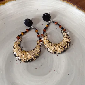 Boucles d'oreilles lune en résine avec feuille d'or et perles sur une assiette en céramique