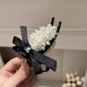 Macro view of a black hair claw clip decorated with elegant white pearl cluster and ribbon bow