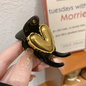 Detailed view of a black hair claw clip featuring a large golden heart embellishment.
