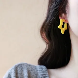 Minimalist yellow star geometric stud earrings featured on model with grey knit sweater