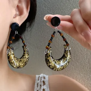 Gros plan détaillé des boucles d'oreilles lune en résine avec feuilles d'or et perles