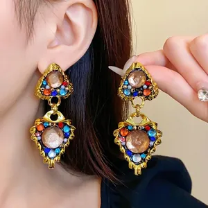 Vintage palace style gold dangling earrings with colorful rhinestones on model.