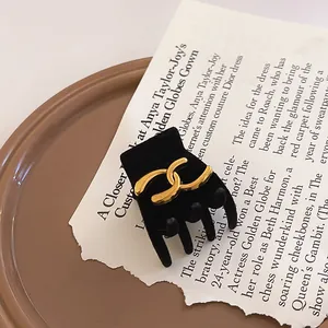 Elegant black velvet hair claw clip featuring a prominent gold interlocking logo detail design