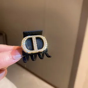 Close-up detail of a black hair claw clip featuring a sparkling rhinestone CD logo design.