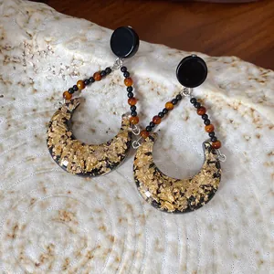 Gros plan sur des boucles d'oreilles lune en résine avec feuilles d'or et perles